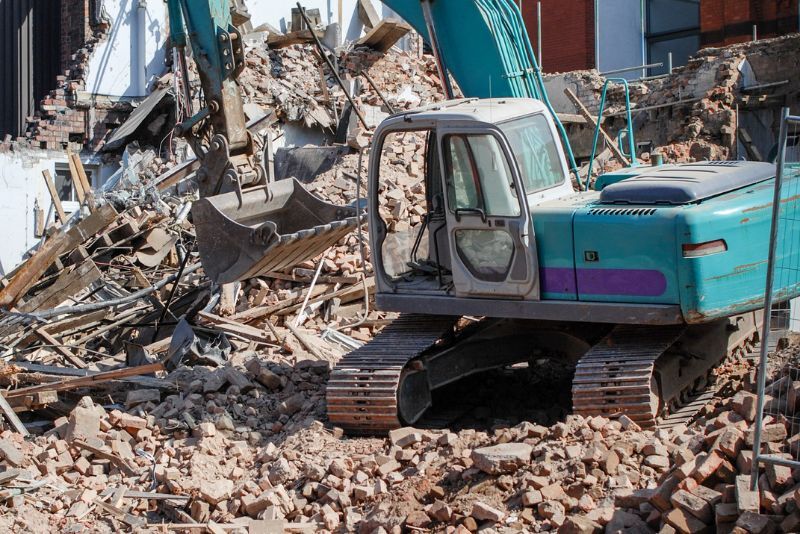 blue excavator machine clearing demolished building